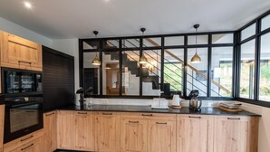 A modern kitchen with wooden cabinets, black appliances, and large windows offering a view of the outdoors. - Le Moulin de Jeannou (PEYRE EN AUBRAC)