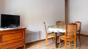 Una habitación con una televisión sobre un aparador de madera, una mesa redonda con mantel floreado y cuatro sillas de mimbre.