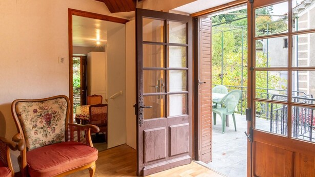 Una habitación con techo de madera, una puerta grande de madera con paneles de vidrio, una silla de mimbre y un cojín rojo.