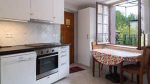 Una cocina con armarios blancos, encimera negra, estufa y ventana con vistas al verdor exterior.