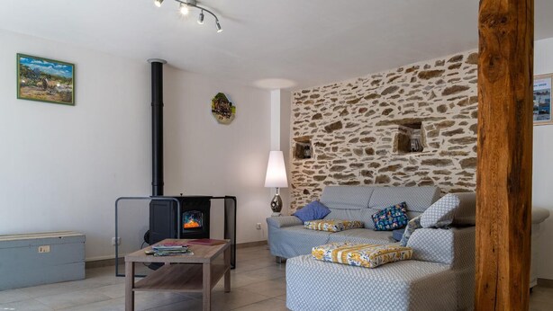 A cozy living room with a stone wall, a fireplace, a sofa, and a table with books. - Gîte Le Pradillou - LES HERMAUX (LES HERMAUX)