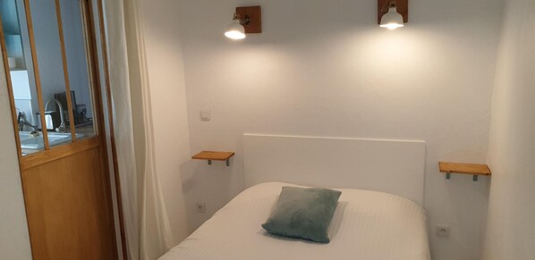 Un dormitorio con una cama, dos mesitas de noche y un ventanal con cortina.