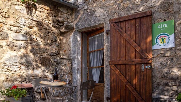 A rustic stone building with a wooden door and a sign for Gîte Lozère.