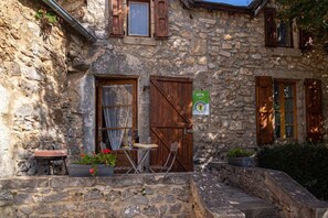 A stone building with a wooden door, a table with chairs, and potted plants.