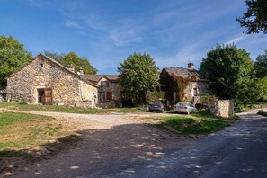 A stone farmhouse with a dirt driveway and parked cars.