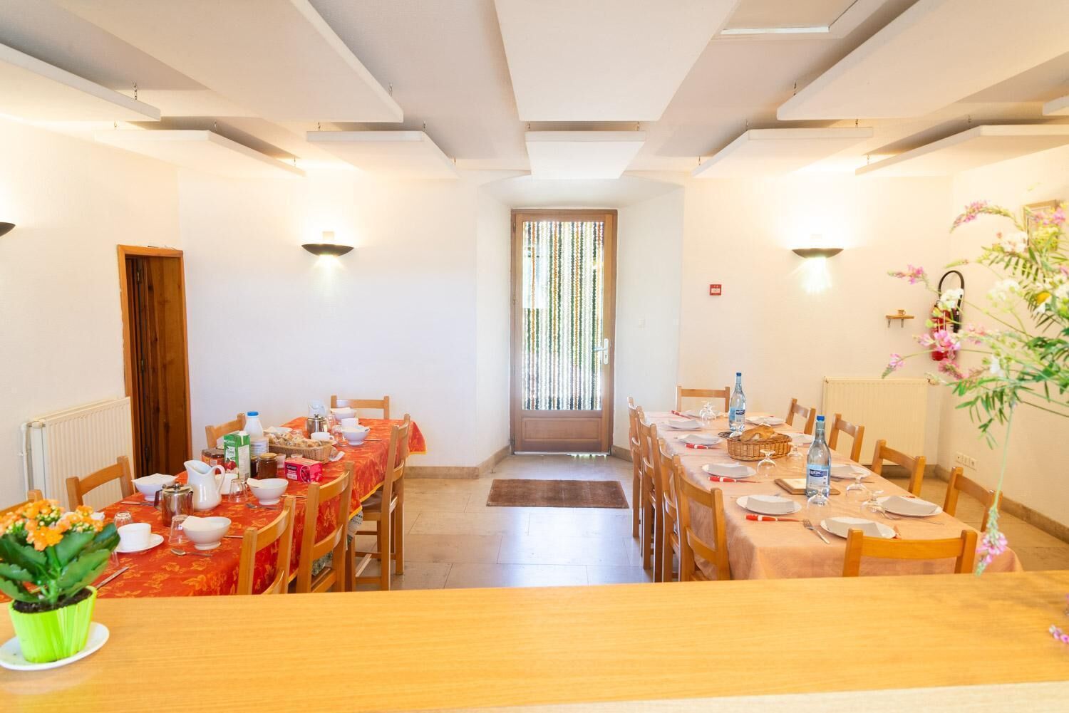 A dining area with two tables set for meals, chairs, a radiator, and a door leading to a balcony.