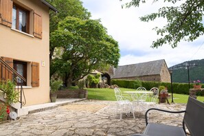 A stone-paved patio with outdoor furniture, a stone building, and a large tree.