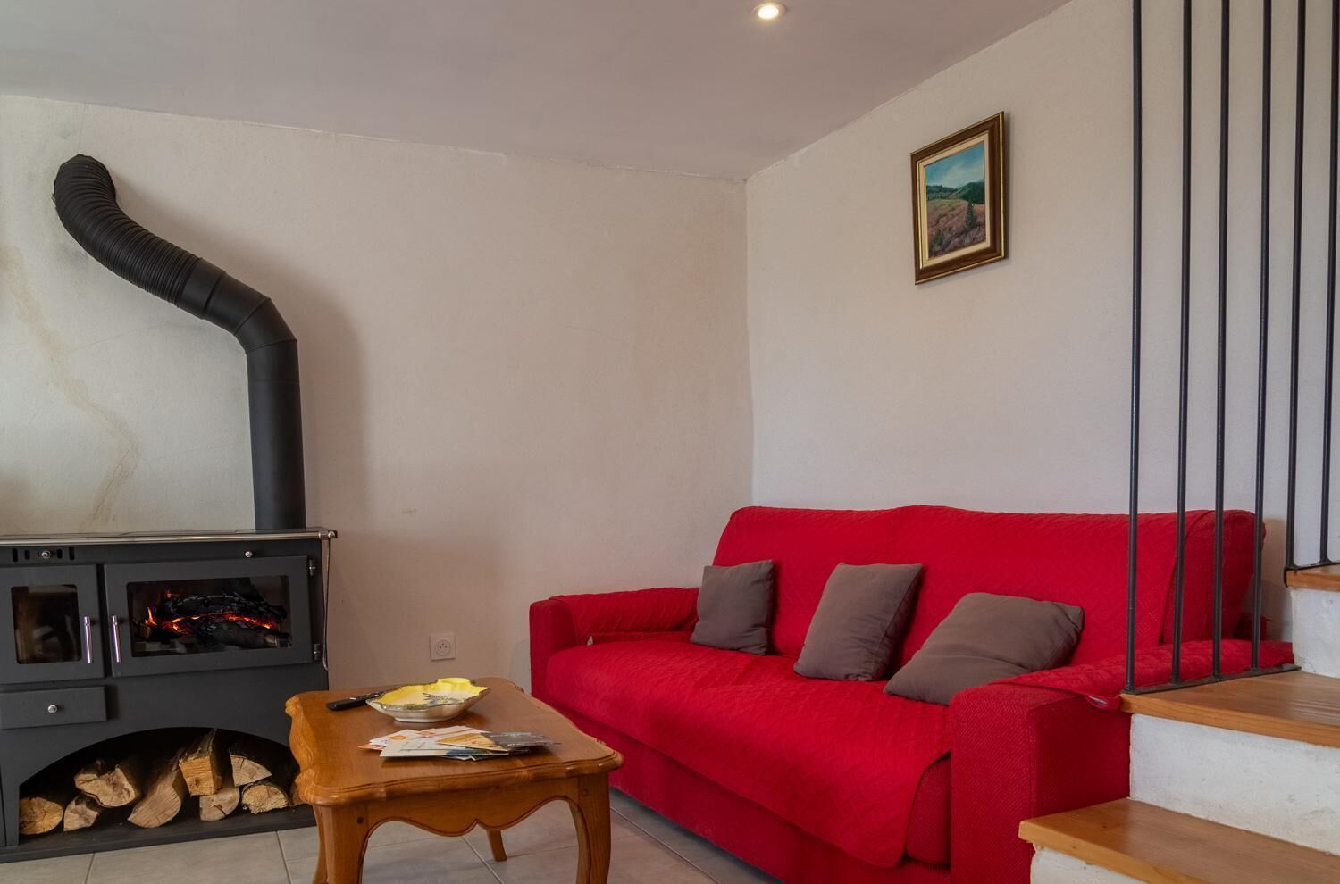 Uma sala de estar com um sofá vermelho, uma mesa de madeira e uma lareira a lenha preta com lenha.