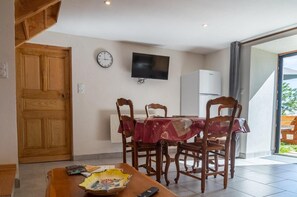 Een eethoek met een houten tafel, stoelen, een klok en een televisie aan de muur.