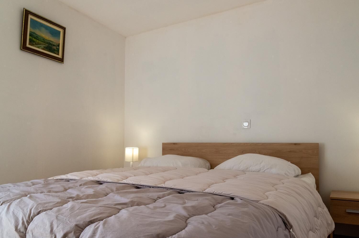 Une chambre à coucher avec un lit, une table de chevet, une lampe fixée au mur et un tableau encadré accroché au mur.