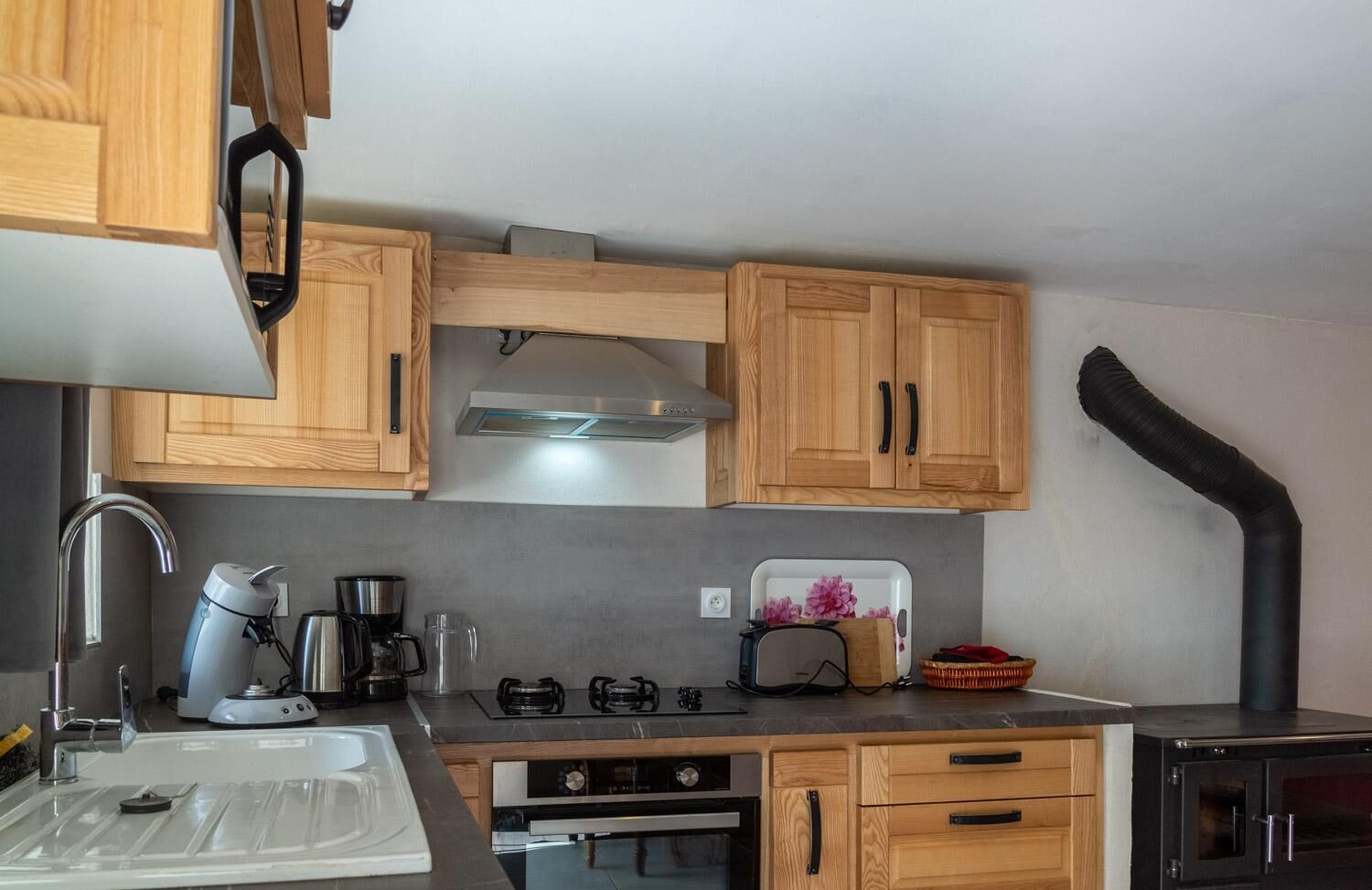 Une cuisine compacte avec des meubles de rangement en bois, une cuisinière à gaz, une machine à café et un grille-pain.