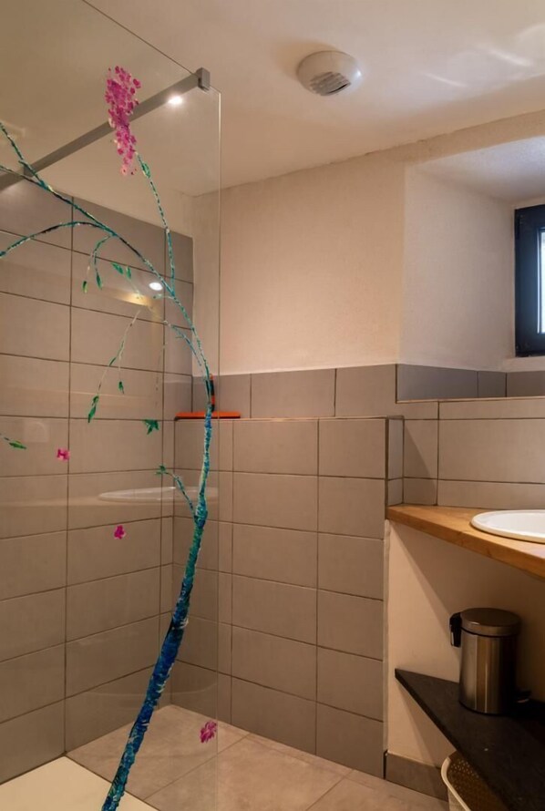 Un baño moderno con cabina de ducha de vidrio, encimera de madera y un cubo de basura a la vista.