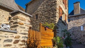 A stone building with a wooden gate, potted plants, and a decorative animal figure. - L'Oustal de Pagat - LES HERMAUX (LES HERMAUX)