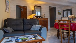 A cozy living room with a sofa, a coffee table with magazines, a wooden cabinet, and a dining area with a red tablecloth. - L'Oustal de Pagat - LES HERMAUX (LES HERMAUX)