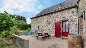 A stone building with a red door, a wooden barrel, and outdoor seating. - Boeuvres-corbinières (GUIPRY MESSAC)