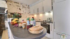A kitchen with a stone wall, white cabinets, and a curved countertop with various food items and kitchen appliances. - Boeuvres-corbinières (GUIPRY MESSAC)