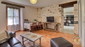A living room with a TV on a wooden stand, a dining area with a table and chairs, and a fireplace. - Boeuvres-corbinières (GUIPRY MESSAC)