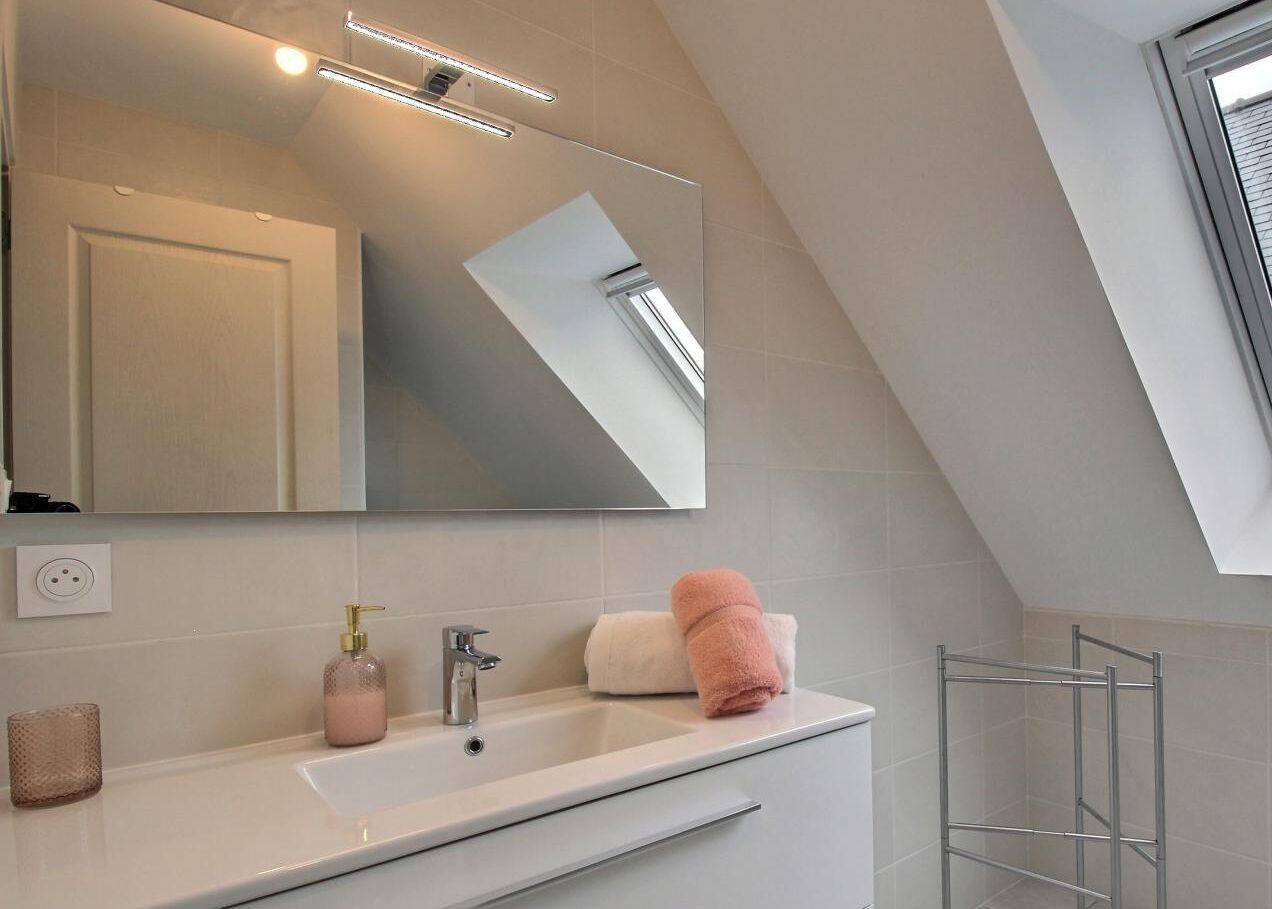 A modern bathroom with a large mirror, a white sink, a towel, and a glass shower enclosure.
