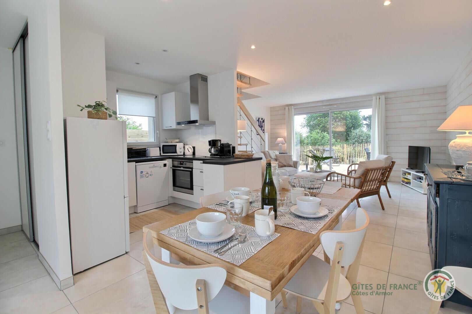 A modern kitchen with white cabinets, a dining area with a wooden table, and a view of the outdoors.