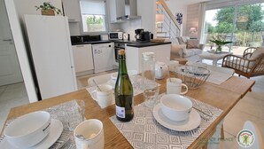 Een moderne keuken met witte kasten, een eethoek met een houten tafel gedekt voor het ontbijt, en een zithoek met een bank en stoelen.