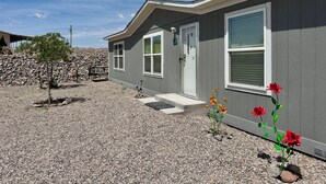 A residential building with a gravel driveway, a small tree, and a flower bed with red flowers. - Spacious 4BR, 2BA, near Lake, Golf Course, and hot springs! (Elephant Butte)