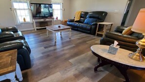Una sala de estar con televisor, dos sofás de cuero, una mesa de centro de madera y una lámpara.