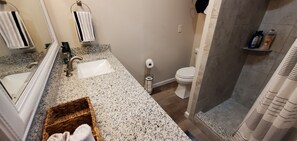 Un baño con encimera de granito, un lavamanos blanco, un inodoro y una zona de ducha.