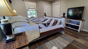 A bedroom with a bed, a television, a lamp, and a window with curtains.
