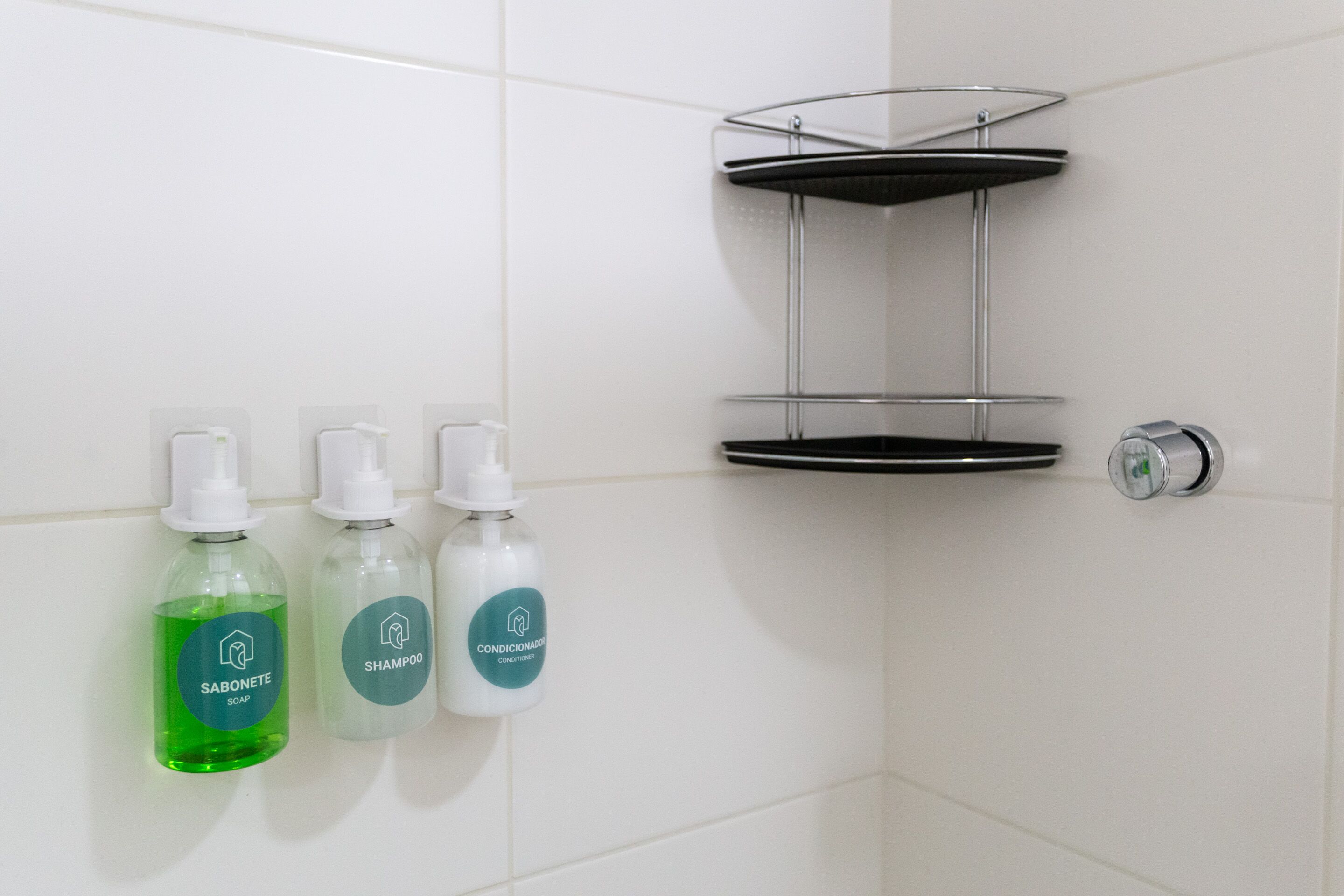 Un baño con tres botellas de jabón y una estantería metálica.
