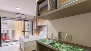 A hotel room with a bed, a small desk with a glass, a red chair, and a balcony with a red chair. - Studio Aurora Paulista 606  (São Paulo)