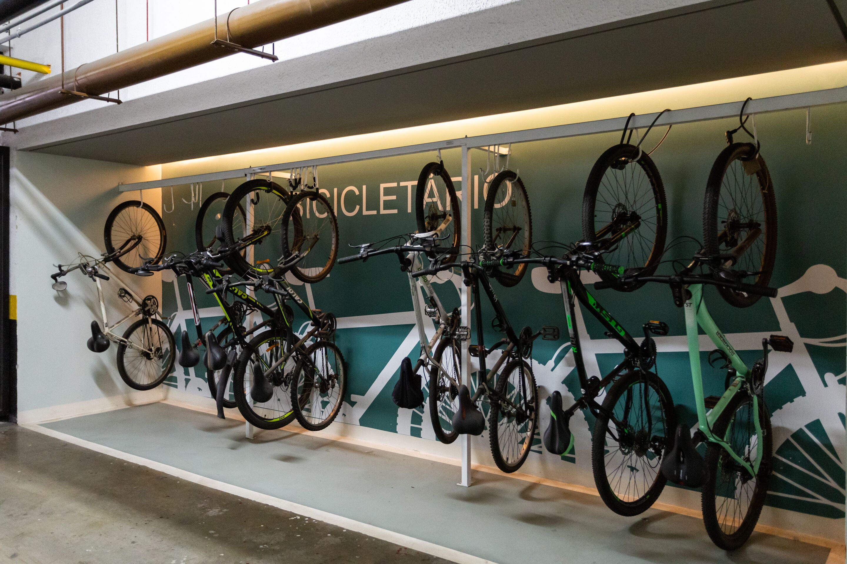 A bike rental station with multiple bicycles mounted on a wall, a clean floor, and a green wall with a mountain design.