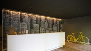 A reception desk with a cityscape mural, a framed certificate, and a yellow bicycle. - Studio Aurora Paulista 606  (São Paulo)