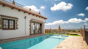 Una piscina al costat d'un edifici amb parets de pedra i teulat de rajoles.