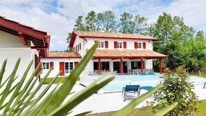 Una casa de dos pisos con piscina, contraventanas rojas y un porche cubierto.