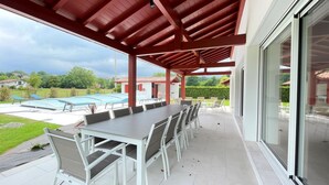 Un patio exterior con piscina, un comedor cubierto con mesa y sillas, y vistas del paisaje circundante.