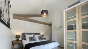 Un dormitorio con cama, mesitas de noche, una lámpara colgante, un armario con puertas de cristal y una obra de arte en la pared.