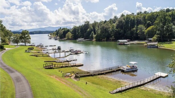 A lakeside property with multiple docks, a grassy area, and a clear view of the lake and surrounding trees. - Lake Chatuge beauty w/private dock, fire pit, pool table, grills and A+ views! (Hayesville)