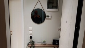 Une petite salle de bain moderne avec une porte blanche, un miroir rond, une petite plante en pot et un appareil noir posé sur un meuble-lavabo en bois.