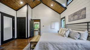 A bedroom with a large bed, wooden ceiling, and a view of the outdoors. - Hot Tub + Modern Cabin + Remote Work Setup (Broken Bow)