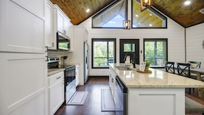 A modern kitchen with white cabinetry, a large island, and a wooden ceiling. - Hot Tub + Modern Cabin + Remote Work Setup (Broken Bow)