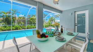 Zona pranzo con vista su piscina e vegetazione tropicale.