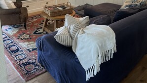 Un salon avec un canapé bleu foncé, un téléviseur à écran plat fixé au-dessus d’une cheminée, une lampe et un tapis à motifs.