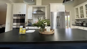 Une cuisine moderne avec des meubles blancs, des appareils en acier inoxydable et un îlot central doté d’un évier et d’objets décoratifs.