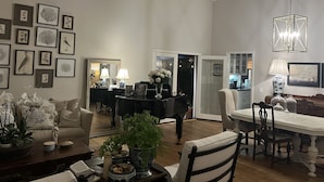 Un vaste salon comprenant un coin repas, une cuisine ouverte sur le salon par une porte, et un couloir menant à une autre pièce.