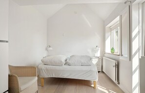 Cozy retreat with a single bed, wicker chair, and natural light pouring in through the window.