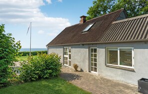 Situated in a lush garden, this house features a sloped roof, skylight, and two windows with white frames.