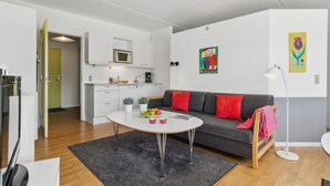 Een modern appartement met een keuken, een grijze bank met rode kussens, een ronde tafel met fruit en een vloerlamp.