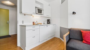 Een compact keukenhoekje met een magnetron, koffiezetapparaat en een klein aanrecht.
