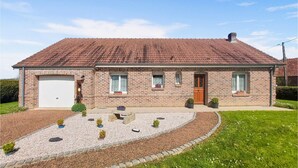 A two-story brick house with a tiled roof, a front garage, and a landscaped front yard with small plants and a gravel pathway. - Awesome home in Quoux-Haut-Maînil with WiFi (Quoux-Haut-Maînil)