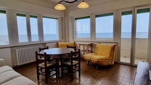 A dining area with a round table and chairs, a yellow armchair, and large windows with a view of the sea. - P012 - Porto Recanati, wonderful three-room apartment facing the sea (Porto Recanati)
